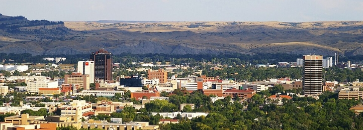 Downtown city skyline with high-rise buildings, green neighborhoods, and rolling hills in the background.