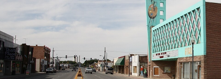 Downtown street lined with brick storefronts and a turquoise theater marquee beneath an overcast sky.
