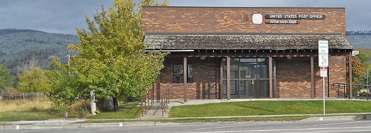 Brick United States Post Office building with trees, sidewalk, and mountains in the background.