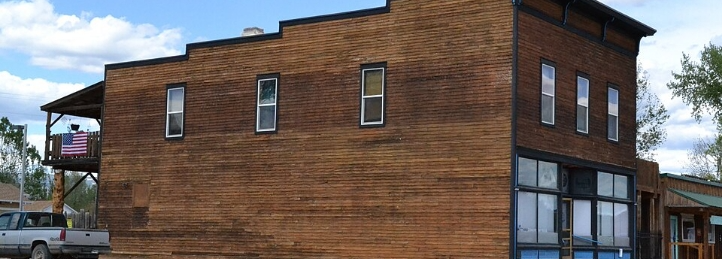 Historic two-story brick building with tall windows, storefront entrances, and an American flag on the side.