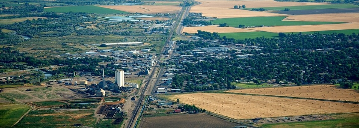 Aerial view of a small rural town surrounded by farmland, fields, and a highway stretching into the distance.