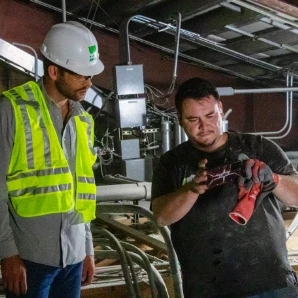 HVAC technicians inspecting a red pipe fitting at a commercial job site.